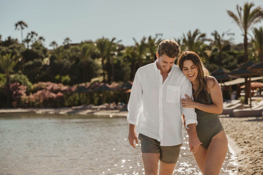 alt:"Fotografía profesional de una pareja de mujer y hombre paseando por la orilla de una playa artificial . Fotografía realizada por By Nau en The Beach, Sotogrande".